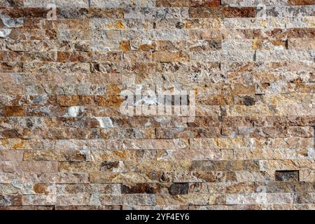 Parete in piastrelle di pietra impilate in varie tonalità di marrone, beige, grigio e bianco. Le pietre sono disposte orizzontalmente con una consistenza ruvida, dando Foto Stock