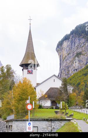 Chiesa con torre a punta di fronte alla parete rocciosa e alla cascata in un paesaggio autunnale, Lauterbrunnen, Svizzera, Europa Foto Stock