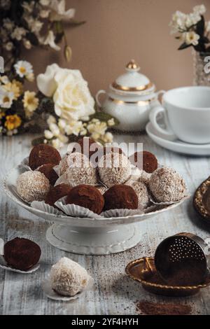 Tiramisù elegantemente disposto, cioccolatini su un piatto di porcellana accanto ai fiori e una tazza Foto Stock