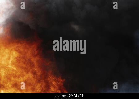 Vista di pericolose fiamme rosse di un enorme fuoco e nuvole di movimento del cielo coperto di fumo nero. Sfocatura, sfocatura del movimento causata da fuoco intenso e temperature elevate Foto Stock