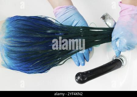 Vista dall'alto del parrucchiere in guanti lavano la testa del cliente con capelli lunghi colore zaffiro dopo il processo di colorazione dei capelli. Lavaggio dei capelli della donna con shampoo i Foto Stock