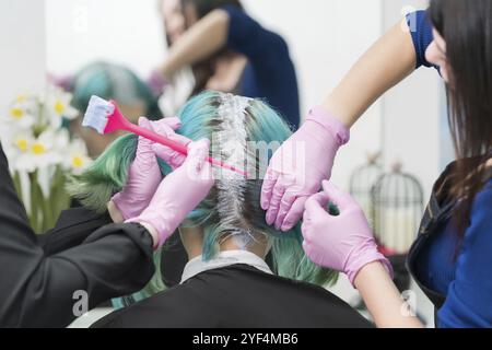 Processo di tintura dei capelli in salone di bellezza. Due parrucchieri professionali che applicano la vernice ai capelli durante la decolorazione delle radici dei capelli Foto Stock