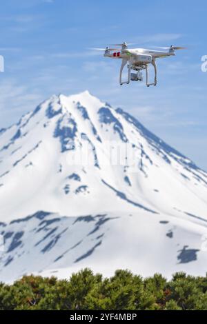 Il quadricottero del drone tecnologico UAV vola nel cielo blu sullo sfondo del picco roccioso del vulcano, filmando video aerei e foto di tutto il mondo dalla vista dall'alto. Kamch Foto Stock