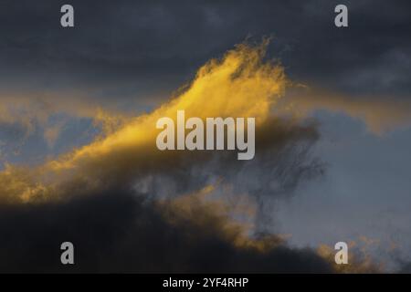 Sbalorditivi soffici nubi di temporale illuminate da raggi scomparsi al tramonto e nubi oscure che galleggiano attraverso il cielo blu soleggiato per cambiare stagione Foto Stock