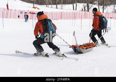 KAMCHATKA, RUSSIA, 28 MARZO 2019: Soccorritori Kamchatka Rescue Squad su sci alpino con barella sci giù pista di monte per primo soccorso medico, evacuazione Foto Stock