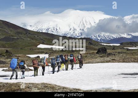 Escursione a Kamchatka: Gruppo di escursionisti con zaino, che si reca in montagna sullo sfondo del bellissimo gruppo di vulcani Klyuchevskaya nelle giornate di sole. Kamchatka Foto Stock