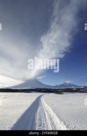 Paesaggio invernale della penisola di Kamchatka: Pista per motoslitte fino al vulcano Klyuchevskoy attivo (Klyuchevskaya Sopka), emissione dal cratere di vulca Foto Stock