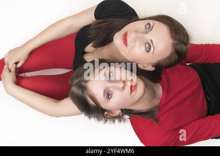 Vista dall'alto di mamma e figlia sedute con le spalle a vicenda e con la testa sulle spalle dell'altra. Entrambe le donne guardano la telecamera. St Foto Stock