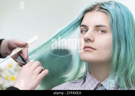 Taglio parrucchieri con forbici lunghi capelli verdi di giovane donna. Cura dei capelli in salone di bellezza professionale Foto Stock