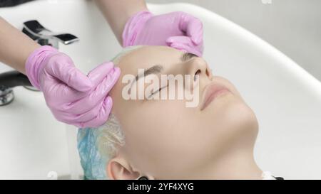 Mani da parrucchiere in guanti rosa che lavano i capelli color smeraldo in un salone di bellezza professionale. Testa di giovane donna con gli occhi chiusi in speciali capelli lavello sa Foto Stock