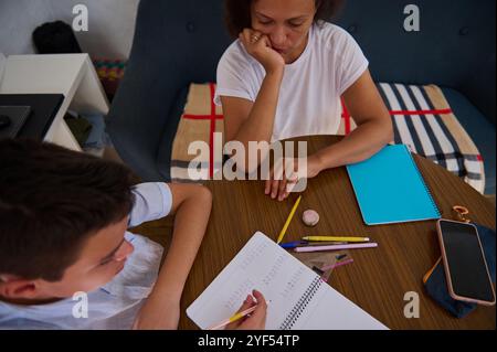 Una madre aiuta suo figlio con i compiti intorno a un tavolo di legno, promuovendo la concentrazione e l'apprendimento in un ambiente accogliente. Foto Stock