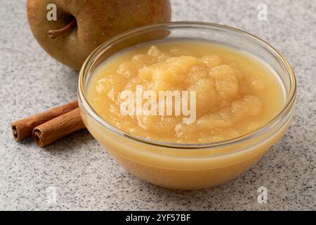 Recipiente di vetro con salsa di mele biologica fatta in casa con cannella e mela fresca sullo sfondo da vicino Foto Stock