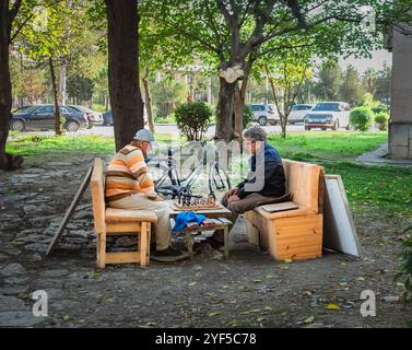 Anziani in pensione che giocano a scacchi su Desk nel parco. Vecchi amici che giocano a domino. Passare del tempo con gli amici può aiutare a migliorare il fisico, la mente Foto Stock