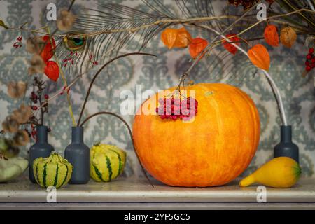 Natura morta autunnale con zucche, fiori e rowan sul mantello. Giorno del Ringraziamento o concetto di halloween. Foto Stock