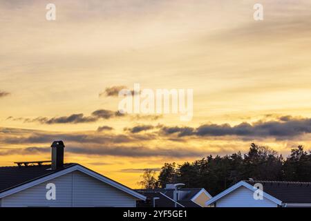 Tetti sagomati e linee d'albero contro il cielo dorato del tramonto con nuvole sparse. Foto Stock