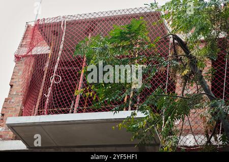 Questa immagine mostra una rete di sicurezza rossa installata su un balcone di un cantiere edile, progettata per evitare cadute accidentali dei lavoratori. La rete garantisce un sa Foto Stock