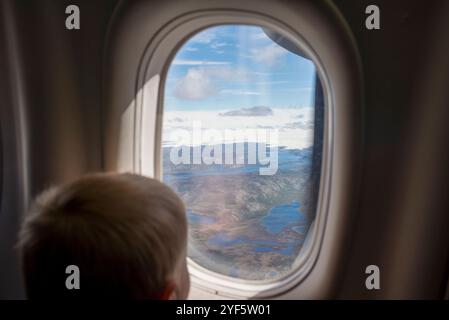 Un bambino che guarda fuori dalla finestra di un aereo, ipnotizzato dal paesaggio mozzafiato della Groenlandia sottostante. Lo splendido sfondo presenta il maestoso Foto Stock