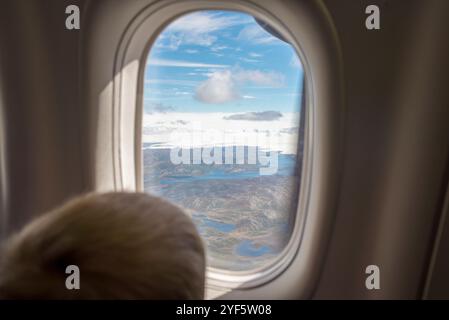 Un bambino che guarda fuori dalla finestra di un aereo, ipnotizzato dal paesaggio mozzafiato della Groenlandia sottostante. Lo splendido sfondo presenta il maestoso Foto Stock