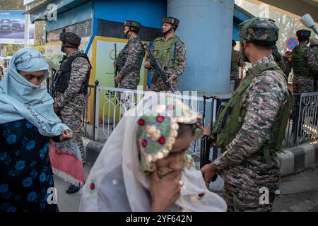 Le donne del Kashmir camminano mentre i soldati paramilitari indiani sono in allerta sul luogo dell'esplosione di granate nel più grande mercato affollato del Kashmir a Srinagar. Un sospetto militante ha lanciato una granata nel più grande mercato affollato del Kashmir, pieno di acquirenti nella città principale della regione contesa dell'Himalaya, ferendo almeno una dozzina di persone, polizia e media locali hanno riferito domenica. L'incidente è avvenuto appena un giorno dopo che un sospetto militante è stato ucciso in uno scontro a fuoco di un giorno a Srinagar, un evento raro in città con una stretta sicurezza. Foto Stock