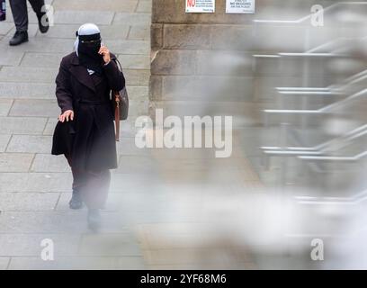 Una donna che indossa gli occhiali e usa un telefono cellulare cammina a Halifax, nel West Yorkshire, indossando il tradizionale abito di un burqa. Crediti: Immagini di mulini a vento/Alamy Live News Foto Stock