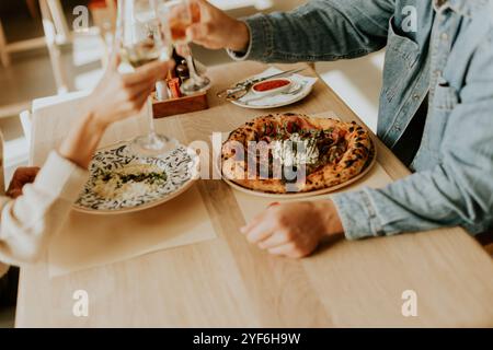 Una coppia solleva i bicchieri con un brindisi gioioso, sorridendo l'un l'altro su un rustico tavolo di legno adornato da piatti vivaci, creando un caldo e io Foto Stock