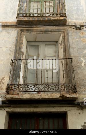 Un primo piano di un antico balcone con ringhiere ornate su un vecchio edificio urbano con pareti in angoscia Foto Stock