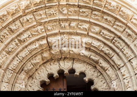 Un arco in pietra splendidamente intagliato incornicia le grandi porte in legno di un'antica chiesa di Obanos, che mostra intricata maestria artigianale. Foto Stock