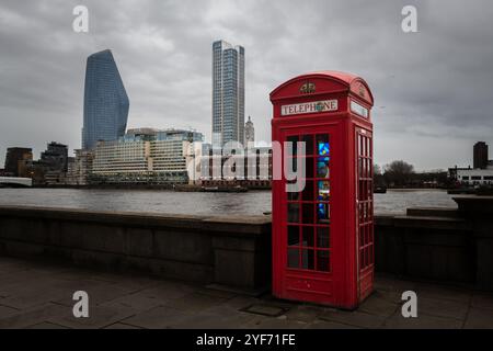Una classica cabina telefonica rossa lungo il Tamigi a Londra con moderni grattacieli sullo sfondo. Foto Stock