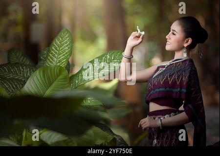 Giovane donna sorridente in abiti tradizionali del Laos in piedi nella foresta che tiene il fiore di frangipani, il Laos Foto Stock