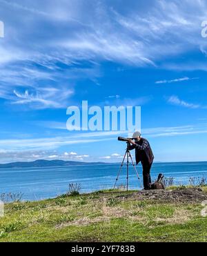 Uomo in piedi vicino al mare di Salish con un telescopio per il bird watching, Victoria, British Columbia, Canada Foto Stock