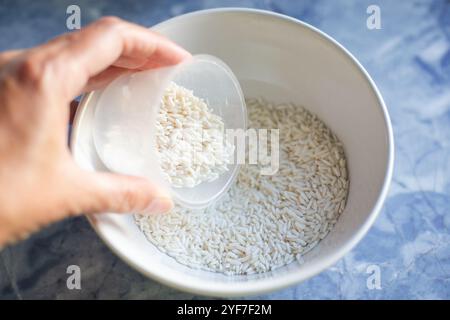 Cuocere il riso. La donna misura un bicchiere di riso e lo versa in una tazza. Foto Stock