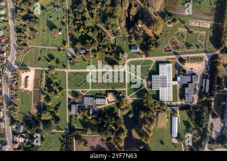 Una vista aerea cattura il paesaggio geometrico di un giardino botanico, caratterizzato da una grande serra, sentieri alberati e diverse sezioni di giardino in un UR Foto Stock