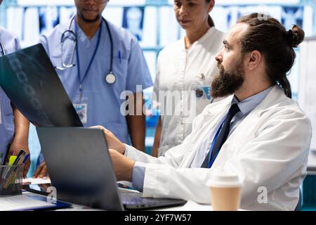 Team diversificato di operatori sanitari che esaminano i risultati dei test di laboratorio in un ambiente clinico, concentrandosi su trattamenti sanitari efficaci. Utilizzo di cartelle cliniche e scansioni a raggi X nell'armadietto. Foto Stock