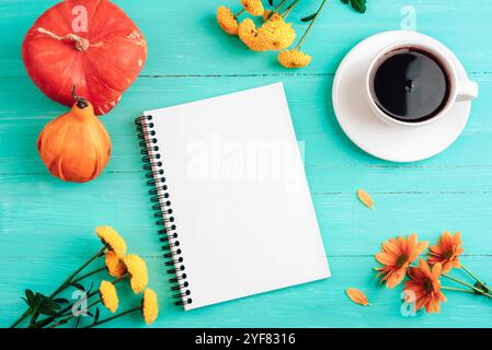 Blocco note vuoto, tazza da caffè, zucche arancioni e fiori su un tavolo di legno blu color tè. Vista dall'alto, posizione piatta, mockup. Foto Stock