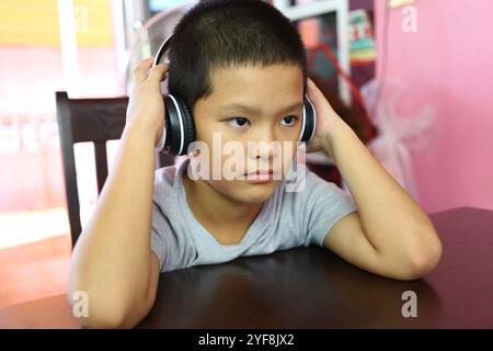 Un ragazzo concentrato che indossa le cuffie si siede a un tavolo, immerso nella sua musica. La sua seria espressione mette in evidenza la profondità della sua concentrazione e la sua Foto Stock