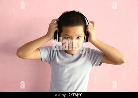 Un ragazzo allegro che indossa le cuffie sorride mentre ascolta la musica in casa. La sua espressione giocosa cattura la gioia e l'emozione di ascoltare il suono. P Foto Stock