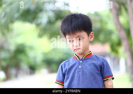 Un ragazzo sta all'aperto, guardando in basso con un'espressione contemplativa. L'ambiente sereno e lo sfondo morbido migliorano il suo umore premuroso. Foto Stock