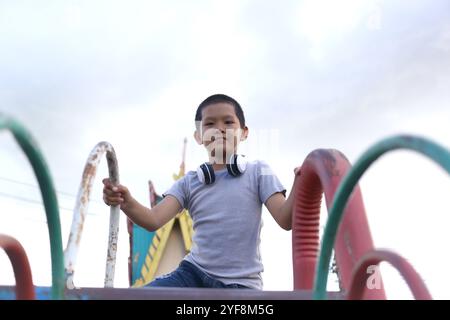 Un ragazzo si diverte a divertirsi in un parco giochi colorato indossando le cuffie. La sua espressione gioiosa cattura l'essenza del gioco all'aperto e dell'infanzia Foto Stock