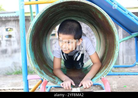 Un bambino ama giocare in un colorato scivolo a tubo per il parco giochi, mostrando gioia e curiosità durante il gioco all'aperto. Perfetto per catturare l'infanzia Foto Stock