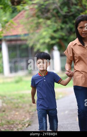 Un bambino cammina mano nella mano con un genitore attraverso un tranquillo percorso all'aperto, mostrando un momento di connessione e calore tra la bellezza della natura. Foto Stock