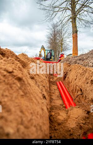 I cavi di rete in tubo corrugato rosso sono interrati per strada. installazione di infrastrutture sotterranee per cavi elettrici. Foto Stock