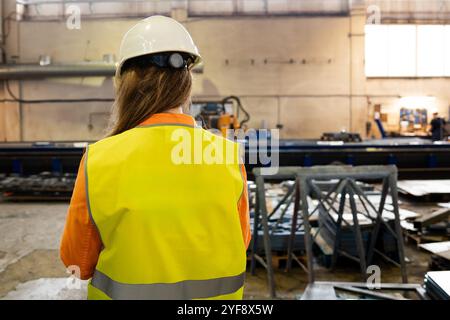 Vista posteriore di una donna industriale ingegnere con smartphone in fabbrica che lavora Foto Stock