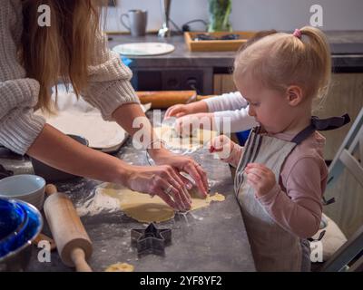 Mamma e figlie condividono un momento di gioia cucinando biscotti a forma di stella in un'accogliente cucina. Risate e farina riempiono l'aria mentre si concentrano Foto Stock