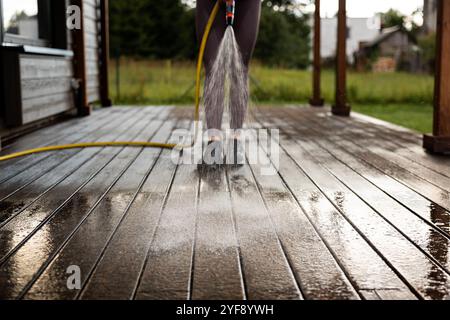 La donna lava una terrazza in legno prima di dipingerla nella sua moderna casa privata Foto Stock