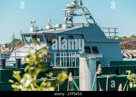 La motovedetta navale ormeggiata al molo della città con attrezzature industriali a bordo sullo sfondo di edifici urbani e un cielo limpido Foto Stock