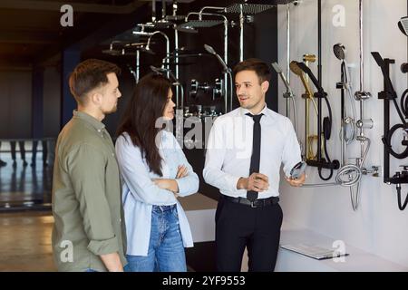 Un venditore vicino alla vetrina del negozio di idraulica che aiuta una giovane coppia a scegliere la doccia. Foto Stock