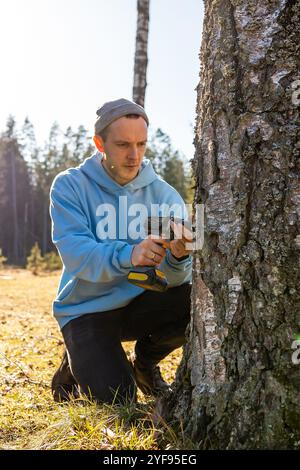 Uomo che sta perforando un albero di betulla per raccogliere linfa fresca in una brillante giornata primaverile Foto Stock