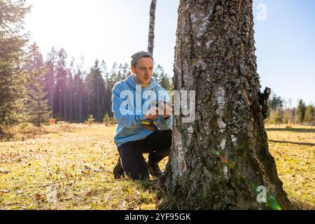 Uomo che sta perforando un albero di betulla per raccogliere linfa fresca in una brillante giornata primaverile Foto Stock