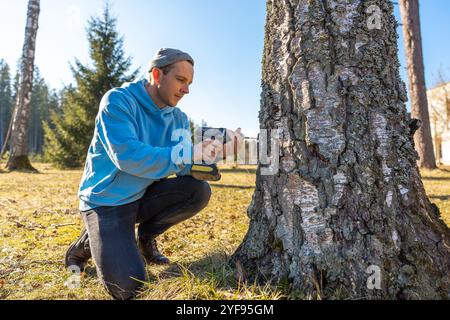 Uomo che sta perforando un albero di betulla per raccogliere linfa fresca in una brillante giornata primaverile Foto Stock