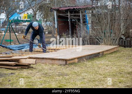 Uomo concentrato che costruisce un ponte di legno nel suo cortile, una scena di lavorazione del legno fai da te e di miglioramento della casa Foto Stock